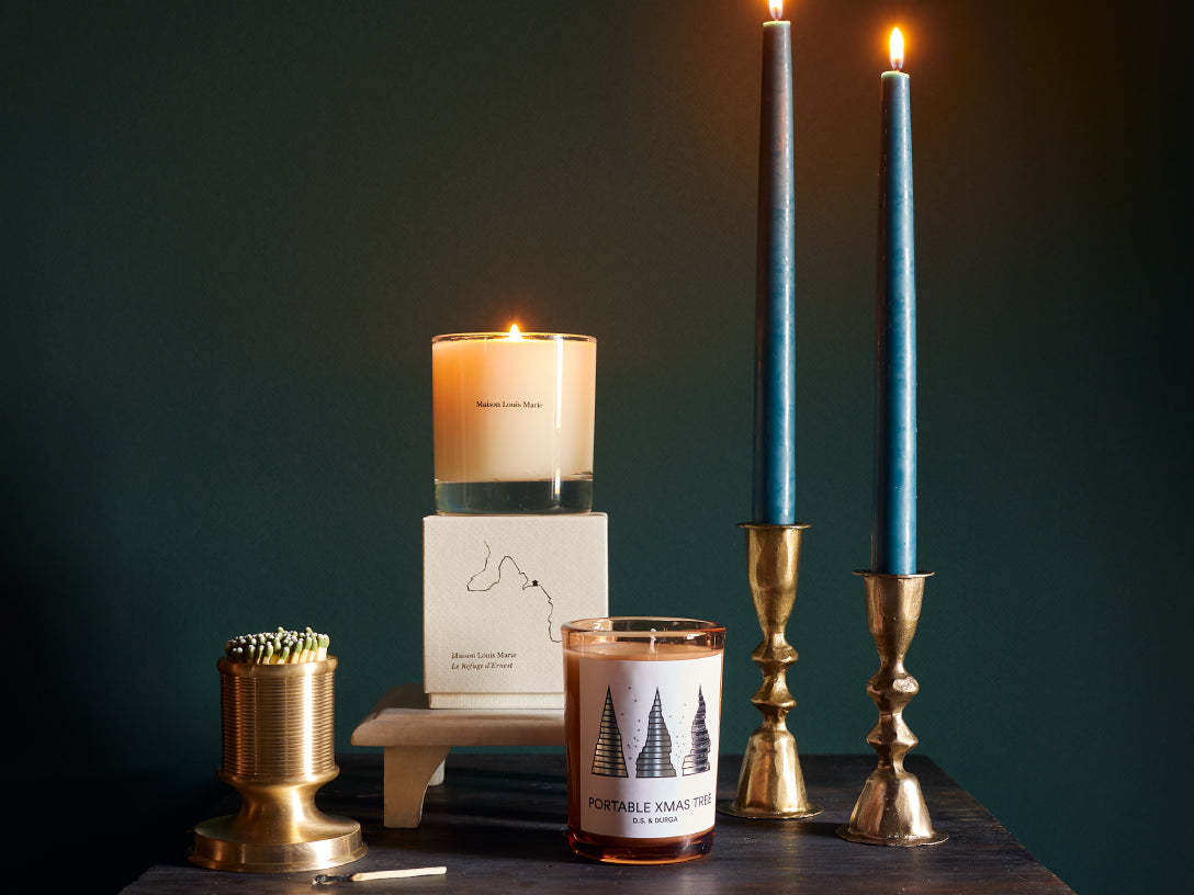 candles and brass match striker next to lit candlesticks in brass holders